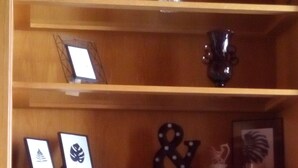 Un estante de madera con diversos objetos decorativos, entre ellos, una obra de arte enmarco, un jarrón y una planta pequeña.