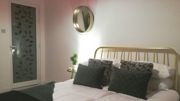Un dormitorio con una cama, un espejo redondo, una mesita con una planta y una puerta con motivos de hojas.