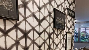 Baño con pared de patrón geométrico, tocador de madera con lavamanos tipo cuenco negro y cuadros en la pared.