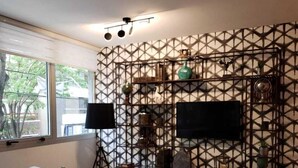 Una habitación de hotel moderna con una pared de estampado geométrico, un televisor de pantalla plana, un sofá, un cabecero de madera y una pequeña mesa redonda.