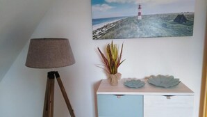 A room with a lamp, a wall-mounted painting of a lighthouse, a plant, and a dresser with drawers. - romantic Oberstübchen (Norden)