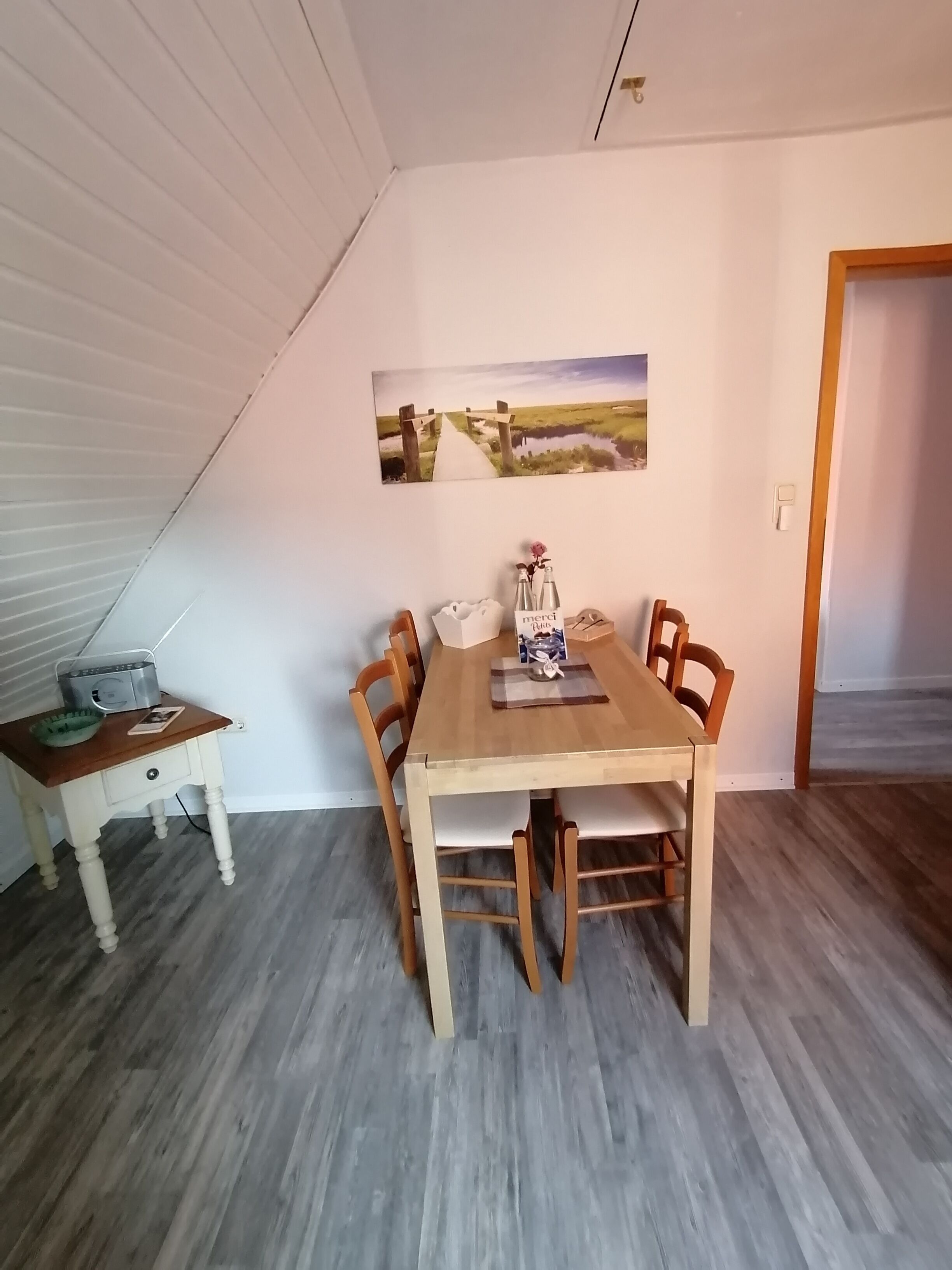 Ein Essbereich mit einem Holztisch, Stühlen, einem kleinen Beistelltisch mit einem Radio und einem Bild an der Wand.