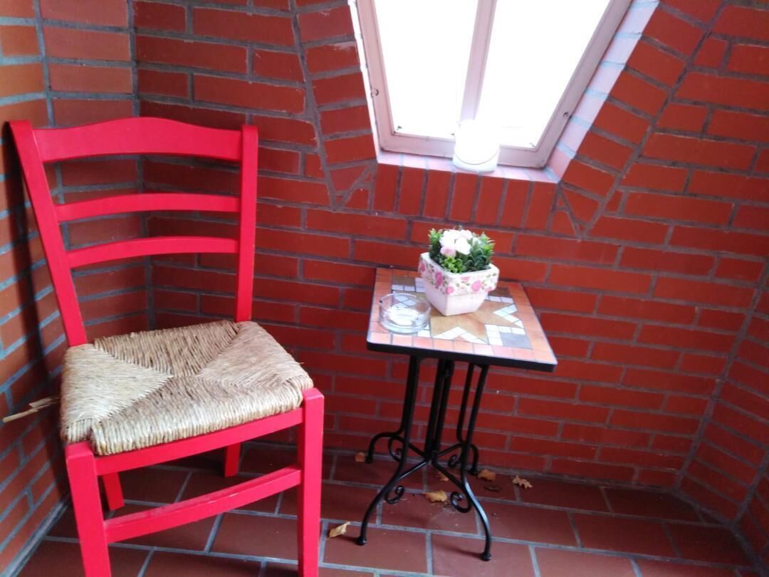 Ein roter Stuhl mit Flechtgeflecht und ein kleiner Tisch mit Blumenarrangement und Kerze.