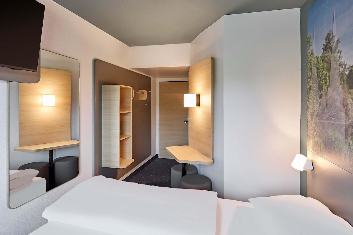 A modern hotel room with a bed, a mirror, a wardrobe, and a painting on the wall.