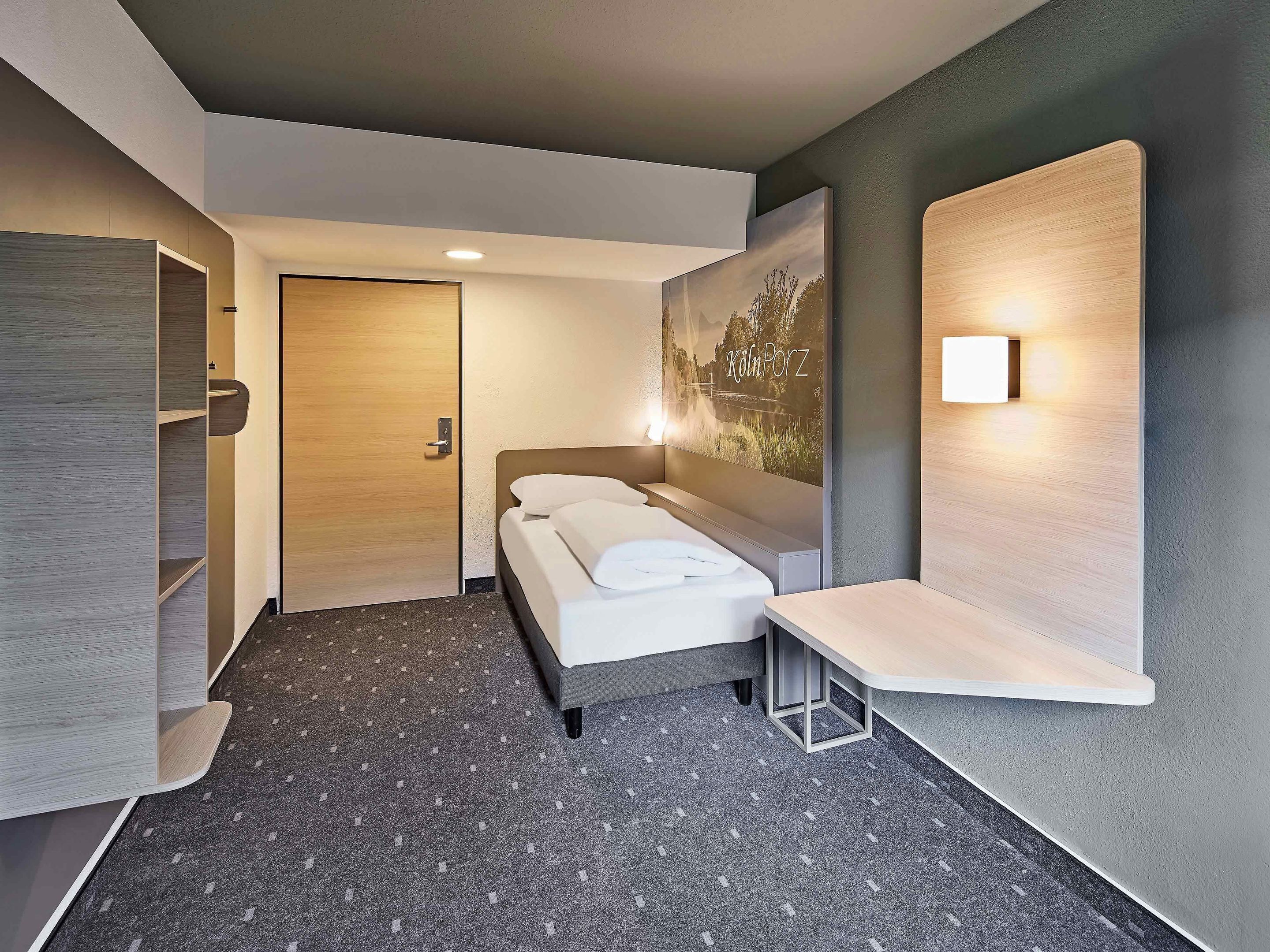 A modern hotel room with a bed, a desk, a wardrobe, and a painting on the wall.