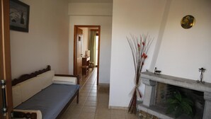 A room with a sofa, a fireplace, and a hallway leading to another room. - Kalliopi Hotel (Minoa Pediada)