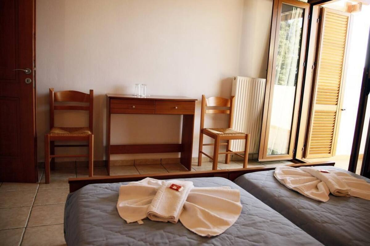 A hotel room with two beds, a wooden desk, two chairs, and a large mirror.