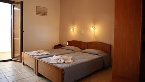 A bedroom with two beds, a wooden headboard, a nightstand, and wall-mounted lights. - Kalliopi Hotel (Minoa Pediada)
