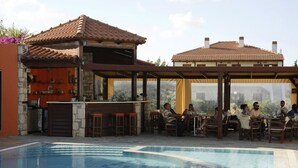 An outdoor pool area with a bar and seating, surrounded by buildings with tiled roofs. - Kalliopi Hotel (Minoa Pediada)