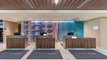 A hotel reception area with three wooden reception desks, a colorful abstract wall mural, and a 'Courtyard by Marriott' sign.