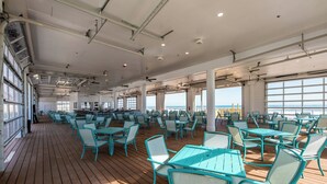 A spacious deck with rows of turquoise tables and chairs, large windows offering views of the sea, and a high ceiling with exposed beams and lighting fixtures. - Courtyard by Marriott South Padre Island (South Padre Island)