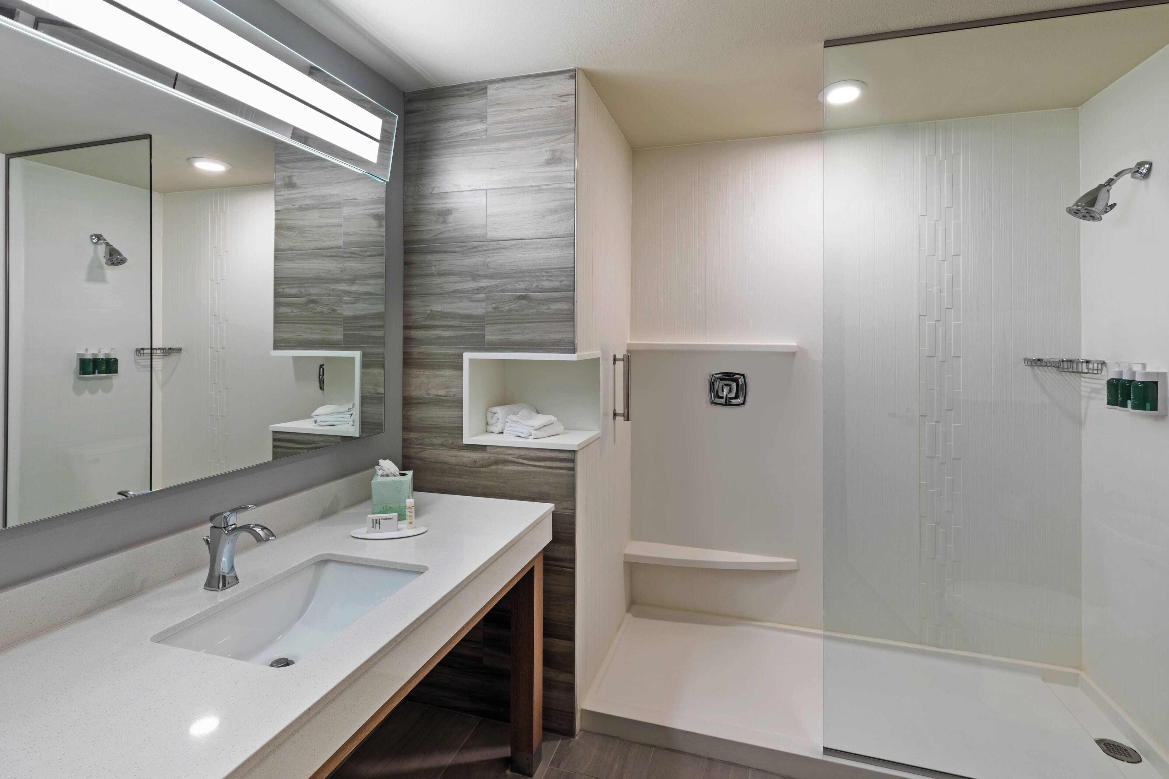 Un bagno moderno con un ampio specchio, un lavandino, una doccia e un mobile contenitore con ripiani.