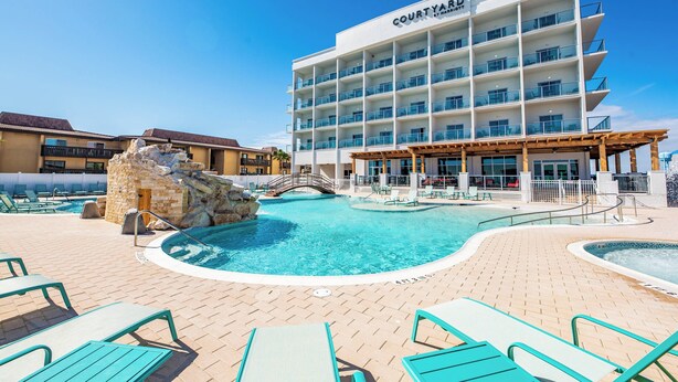 A Courtyard hotel with a swimming pool, outdoor seating, and a stone waterfall feature. - Courtyard by Marriott South Padre Island (South Padre Island)