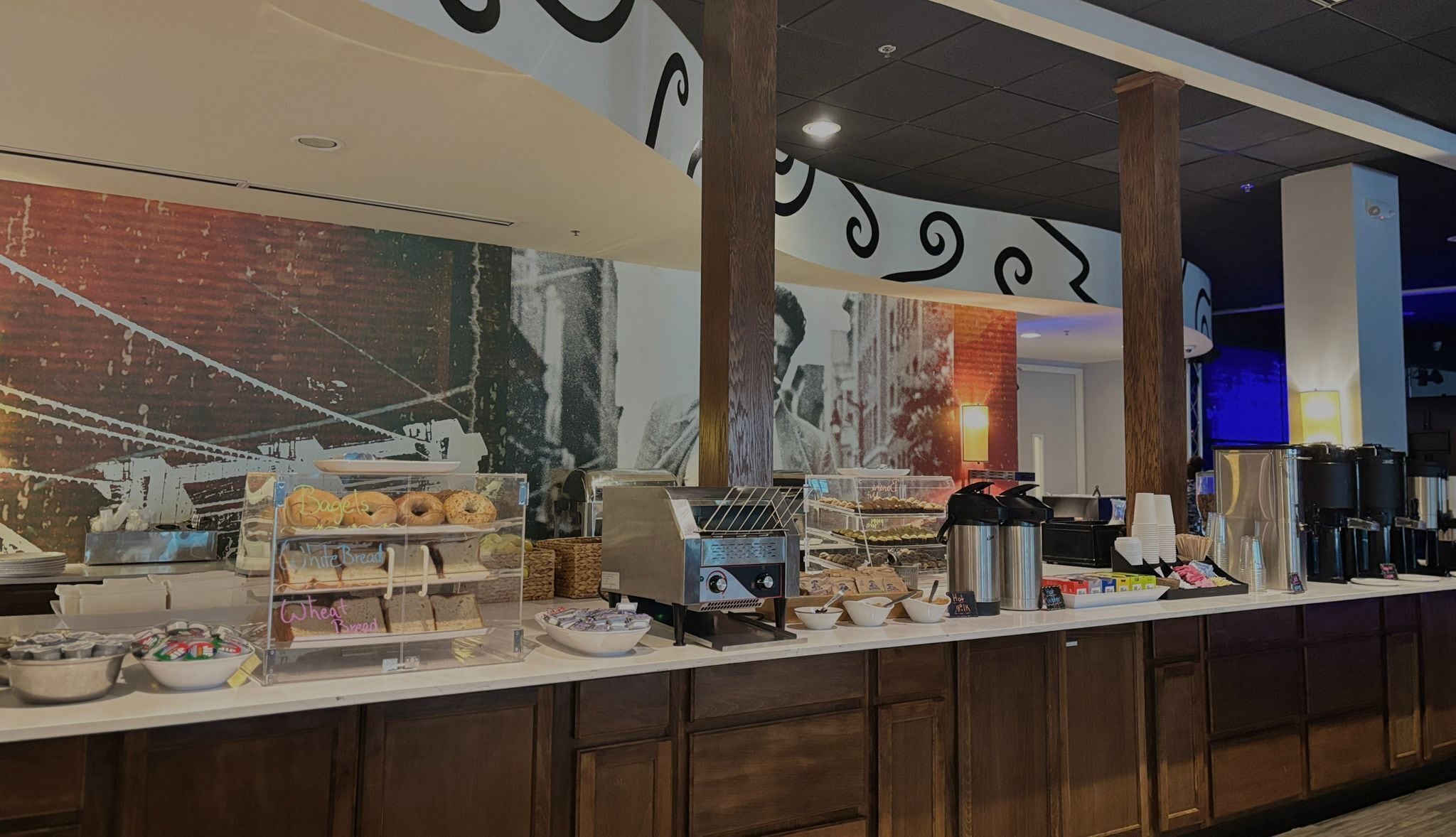 Un comptoir de buffet proposant divers plats, une machine à café et une grande fresque murale.