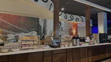 A buffet counter with various food items, a coffee machine, and a large mural on the wall.