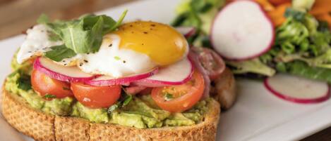 A sandwich with avocado, tomatoes, radishes, and a poached egg on a slice of bread, accompanied by a side salad.