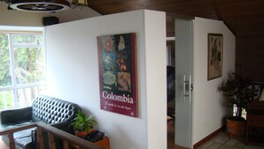 Una sala de estar con un sofá de cuero negro, una mesa de centro de madera y una planta en maceta. Hay un cartel en la pared y una puerta que da a otra habitación.
