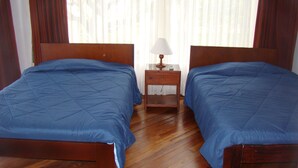 Una habitación con dos camas, una mesita de noche con lámpara y una ventana con cortinas.