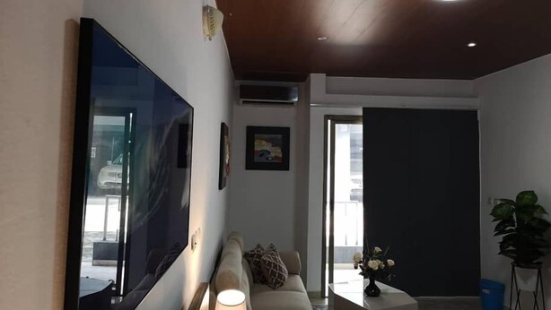 Una sala de estar moderna con un televisor de pantalla plana grande, un sofá, una mesa de centro y una lámpara.