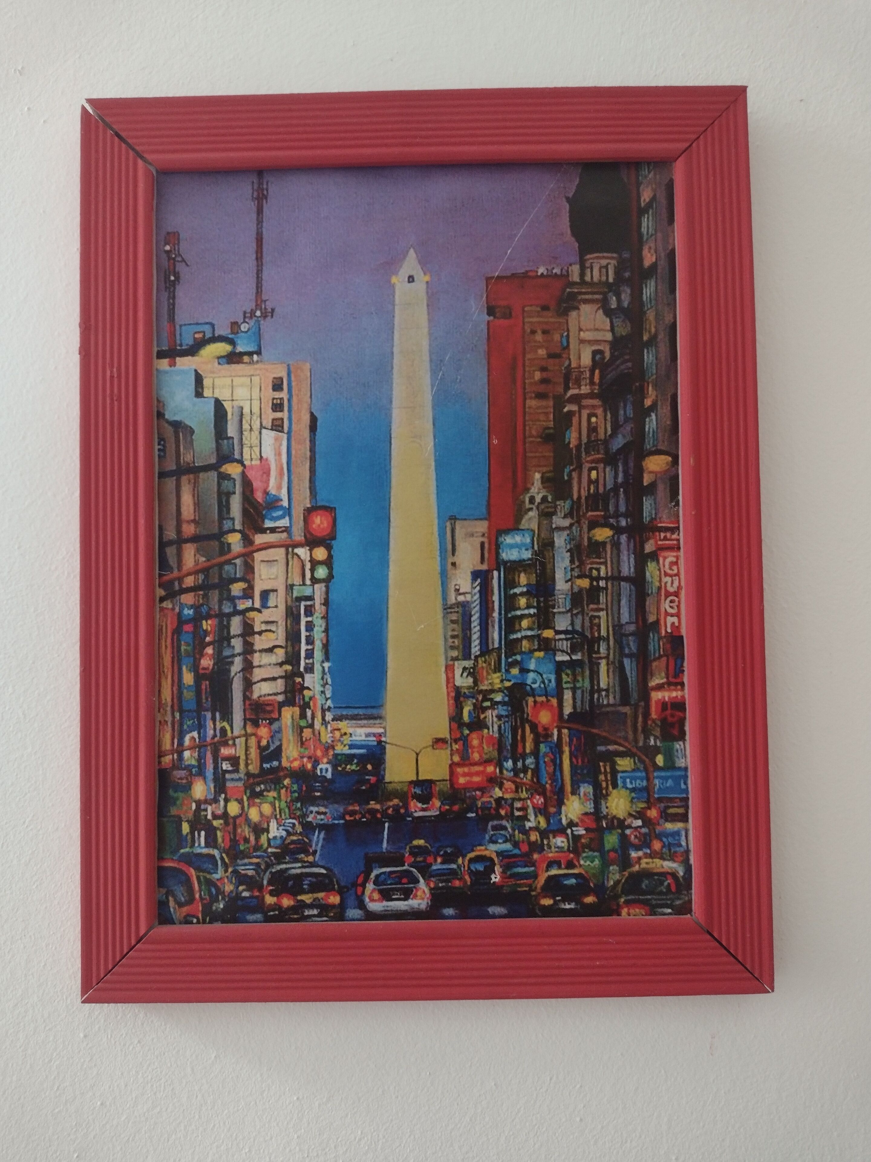 A framed painting of a busy cityscape with tall buildings and a prominent obelisk.