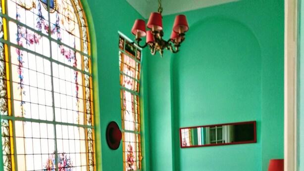 Um quarto com uma grande janela de vitrais, um sofá vermelho, cadeiras estampadas e um piso com padrão.
