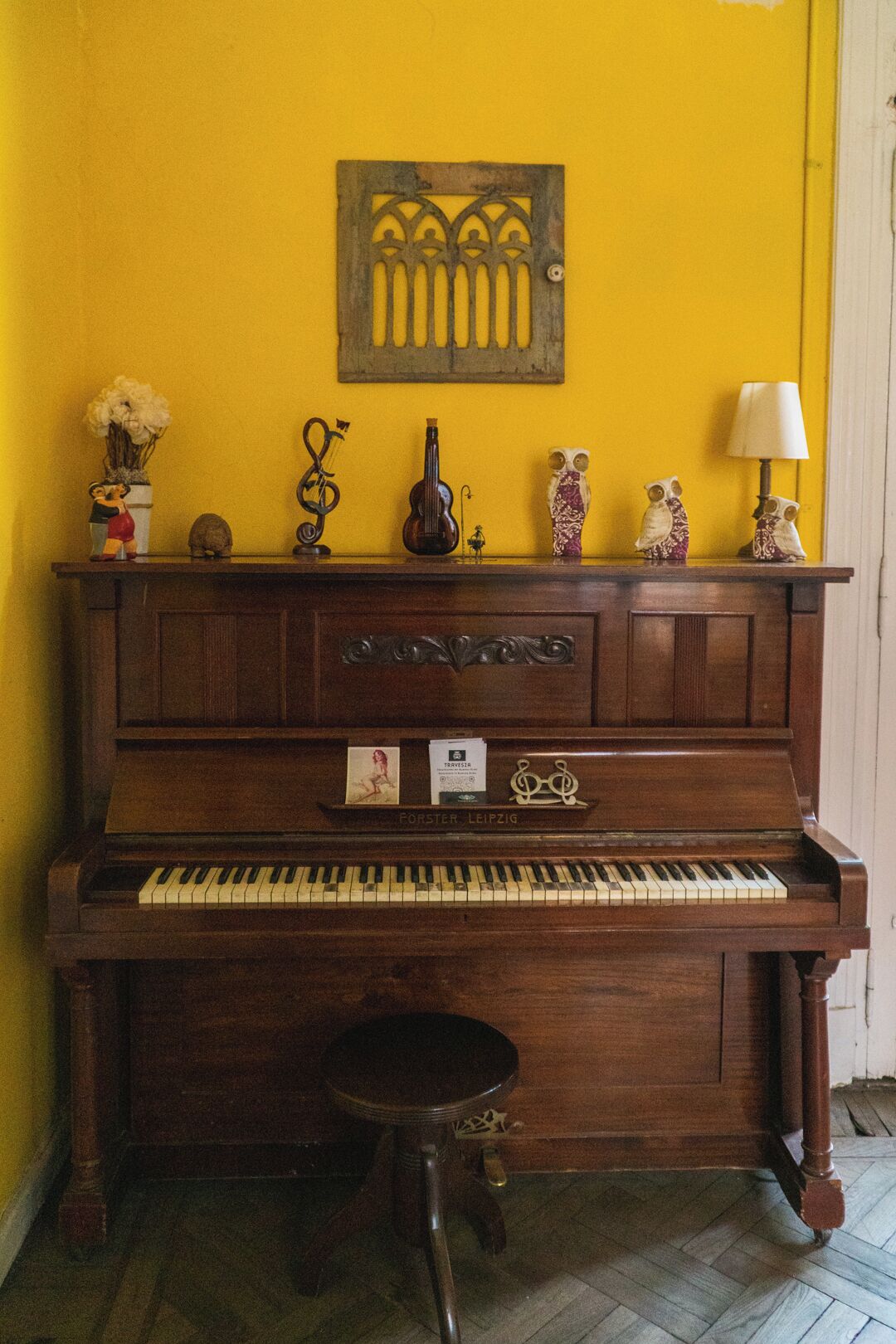 A wooden piano with a bench, a decorative wall piece above it, and various small items on the piano's top.