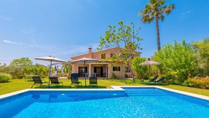 Una piscina con sillas de descanso, una casa con patio y palmeras.