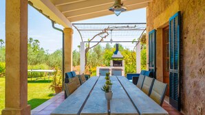 Un patio al aire libre con una mesa larga, sillas, una planta en maceta y una parrilla.