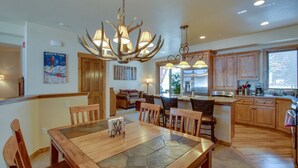A spacious kitchen with wooden cabinets, a dining area with a large table, and a chandelier with antler-shaped lights.