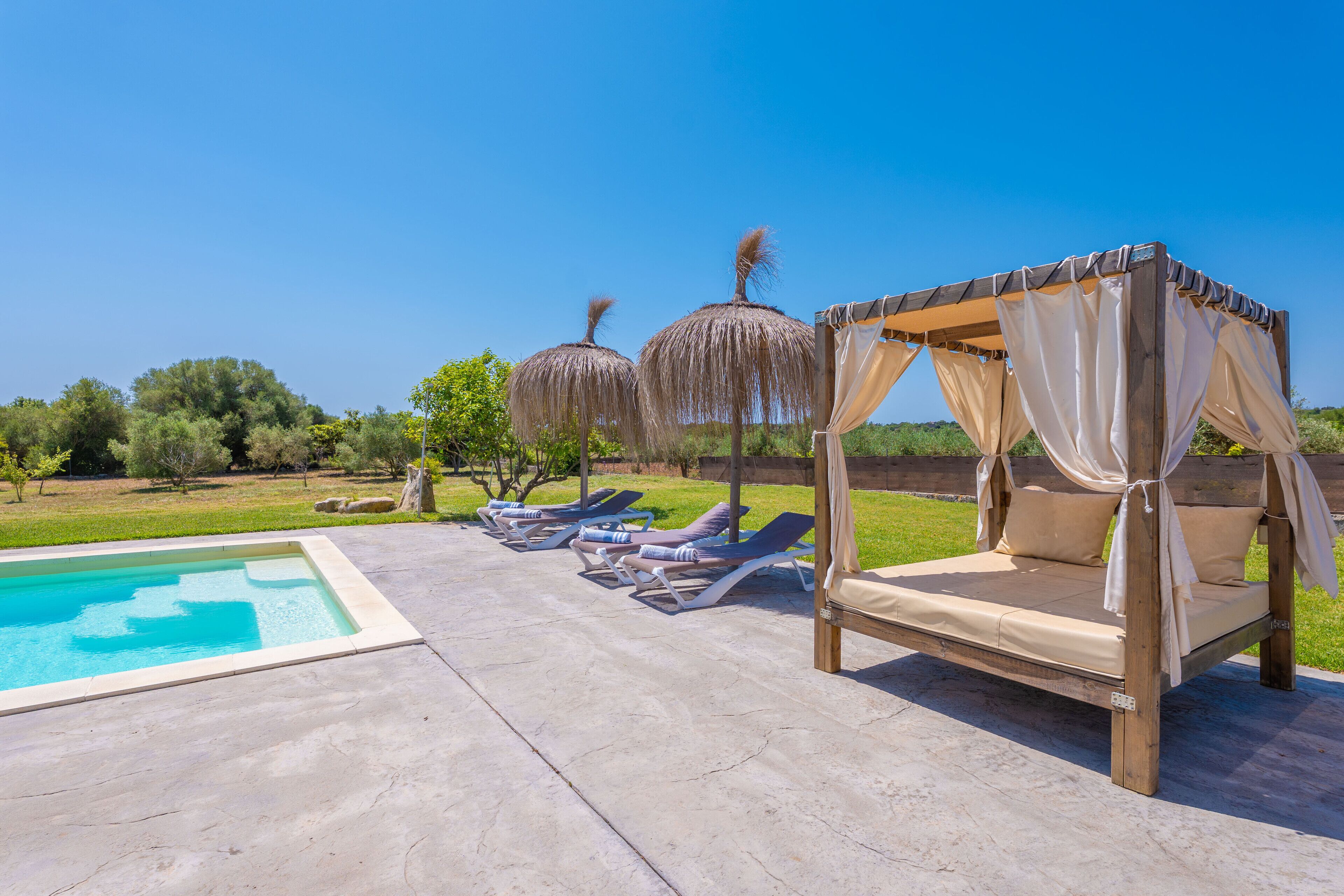 A poolside area with a wooden canopy bed, lounge chairs, and a pool.