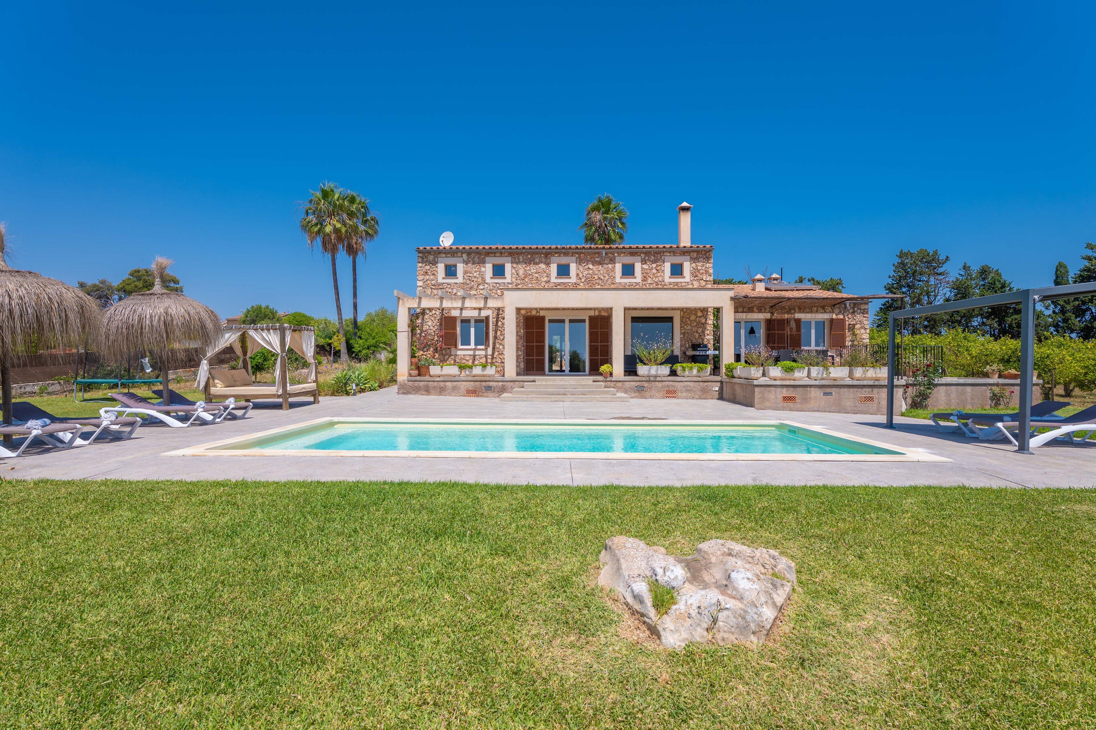Una casa de dos pisos con una piscina, un patio con sillas de descanso y una gran roca al frente.