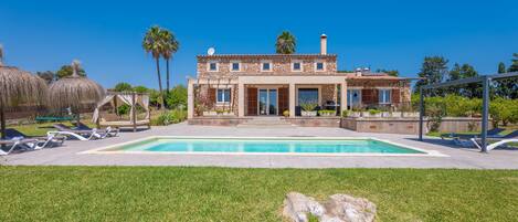 Una casa de dos pisos con una piscina, un patio con sillas de descanso y una gran roca al frente.