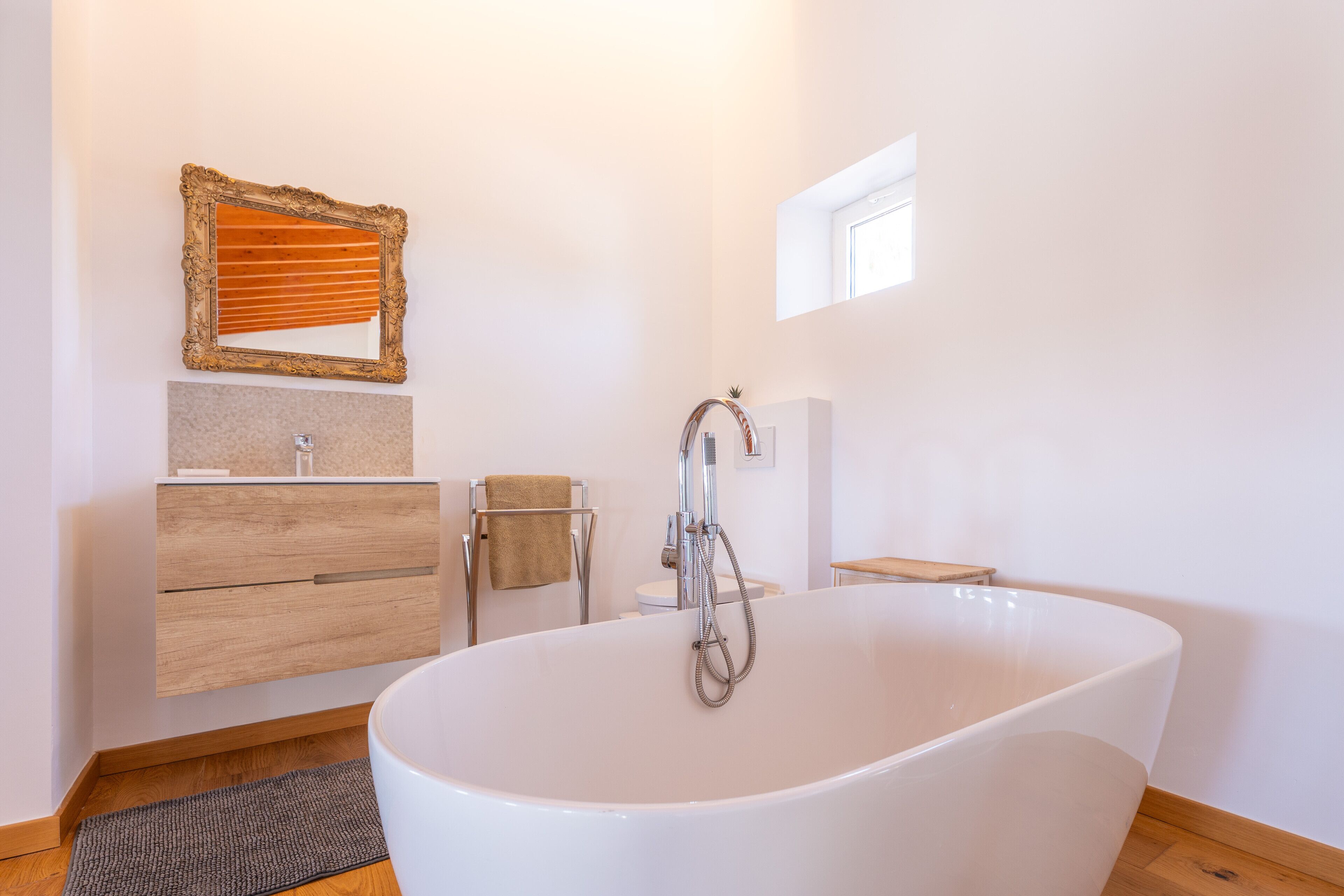 Ein modernes Badezimmer mit einer freistehenden Badewanne, einem hölzernen Waschtisch und einem Spiegel mit aufwändigem Rahmen.