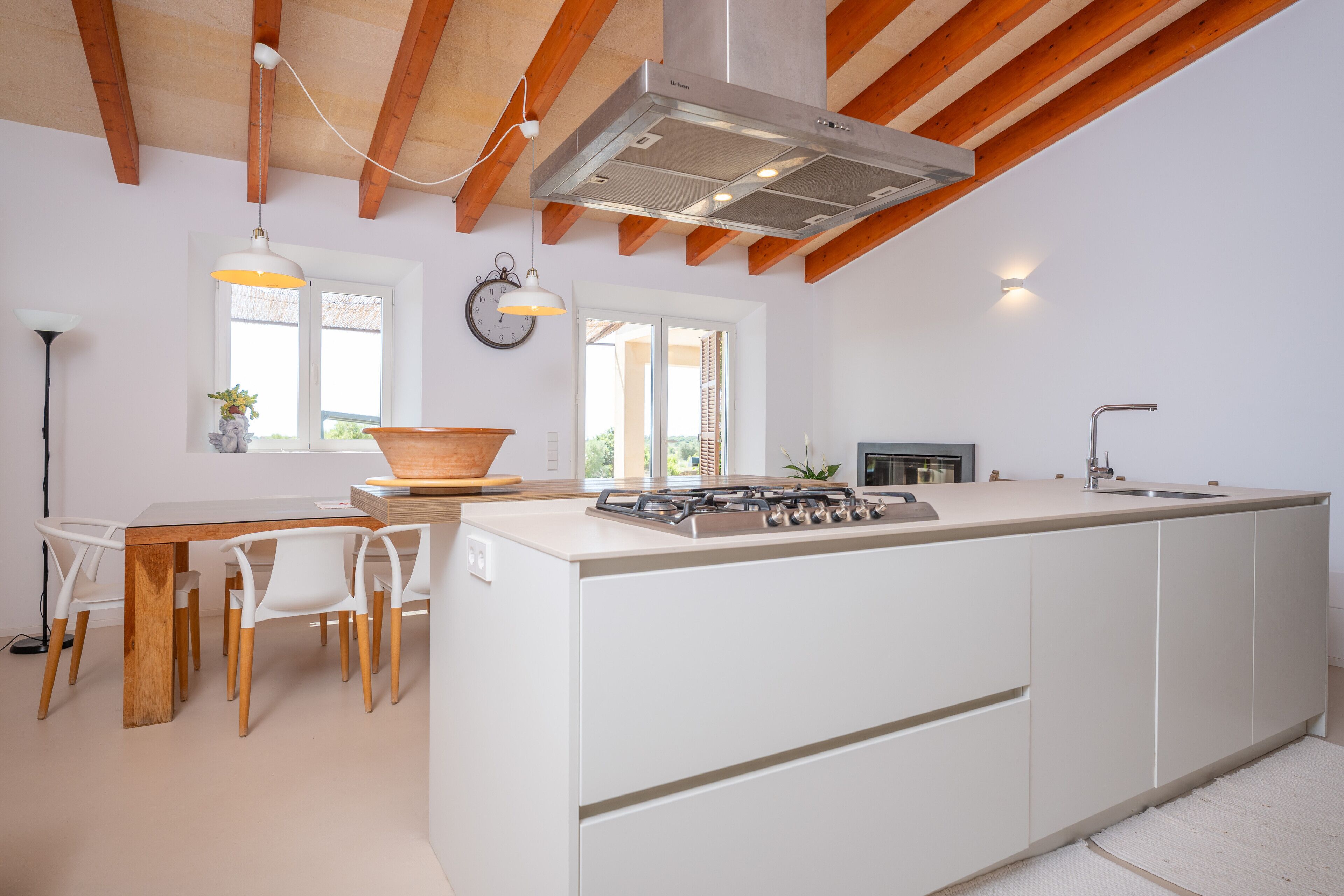 A modern kitchen with a central island, wooden ceiling beams, and a large window providing natural light.
