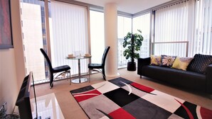 Een moderne woonkamer met een zwarte leren bank, een glazen salontafel, twee zwarte fauteuils en een grote potplant.