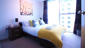 Een slaapkamer met een bed, een nachtkastje, een kunstwerk aan de muur en een raam met gordijnen.