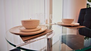 Een eetruimte met een glazen tafel, twee kommen, borden en een wijnglas.