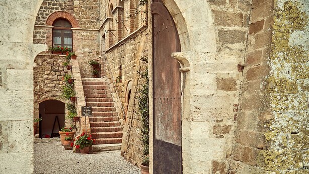 Un estrecho callejón de piedra con una puerta de madera, paredes de piedra y macetas con plantas.