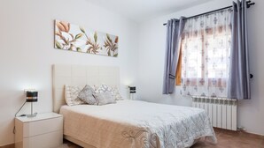 Ein Schlafzimmer mit Bett, Nachttischen, einem Heizkörper und einem Fenster mit Vorhängen.