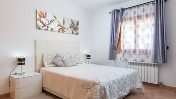 A bedroom with a bed, nightstands, a radiator, and a window with curtains.