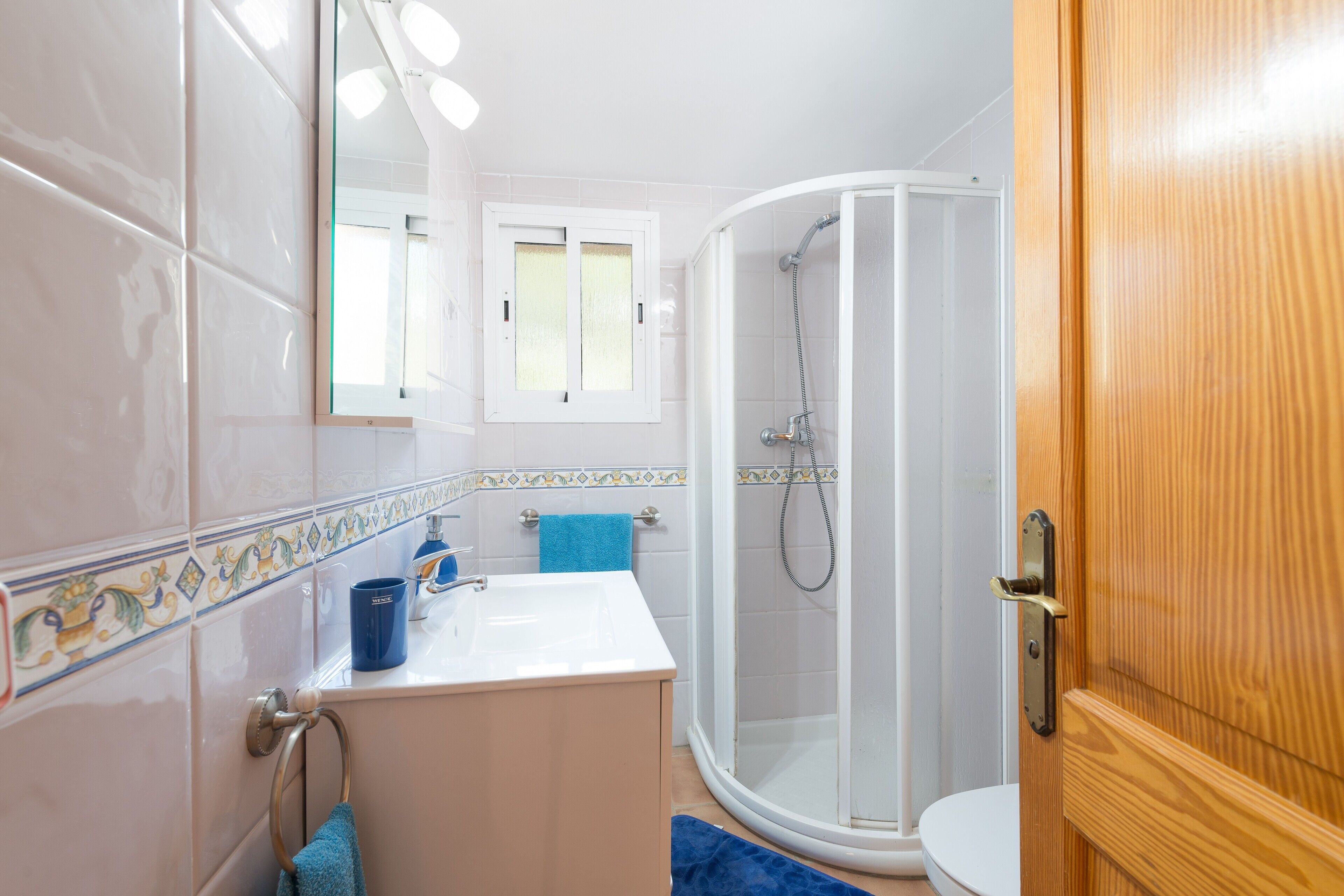 Un baño con un lavamanos blanco, una toalla azul, un cerramiento de ducha de vidrio y una puerta de madera.