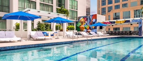 A swimming pool with blue lane dividers, white lounge chairs, and blue umbrellas.