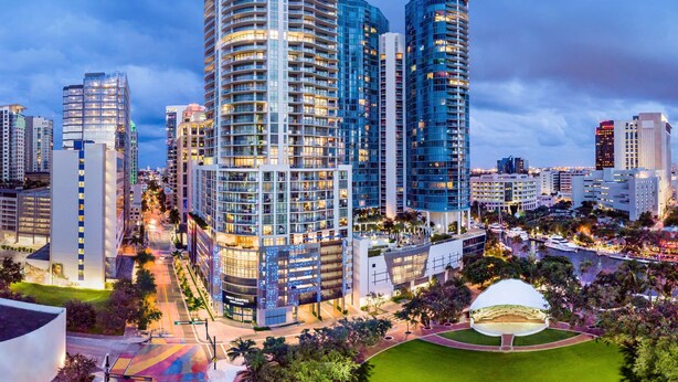 A modern high-rise building with a curved facade, surrounded by other high-rise buildings, a well-maintained lawn, and a large white dome structure.
