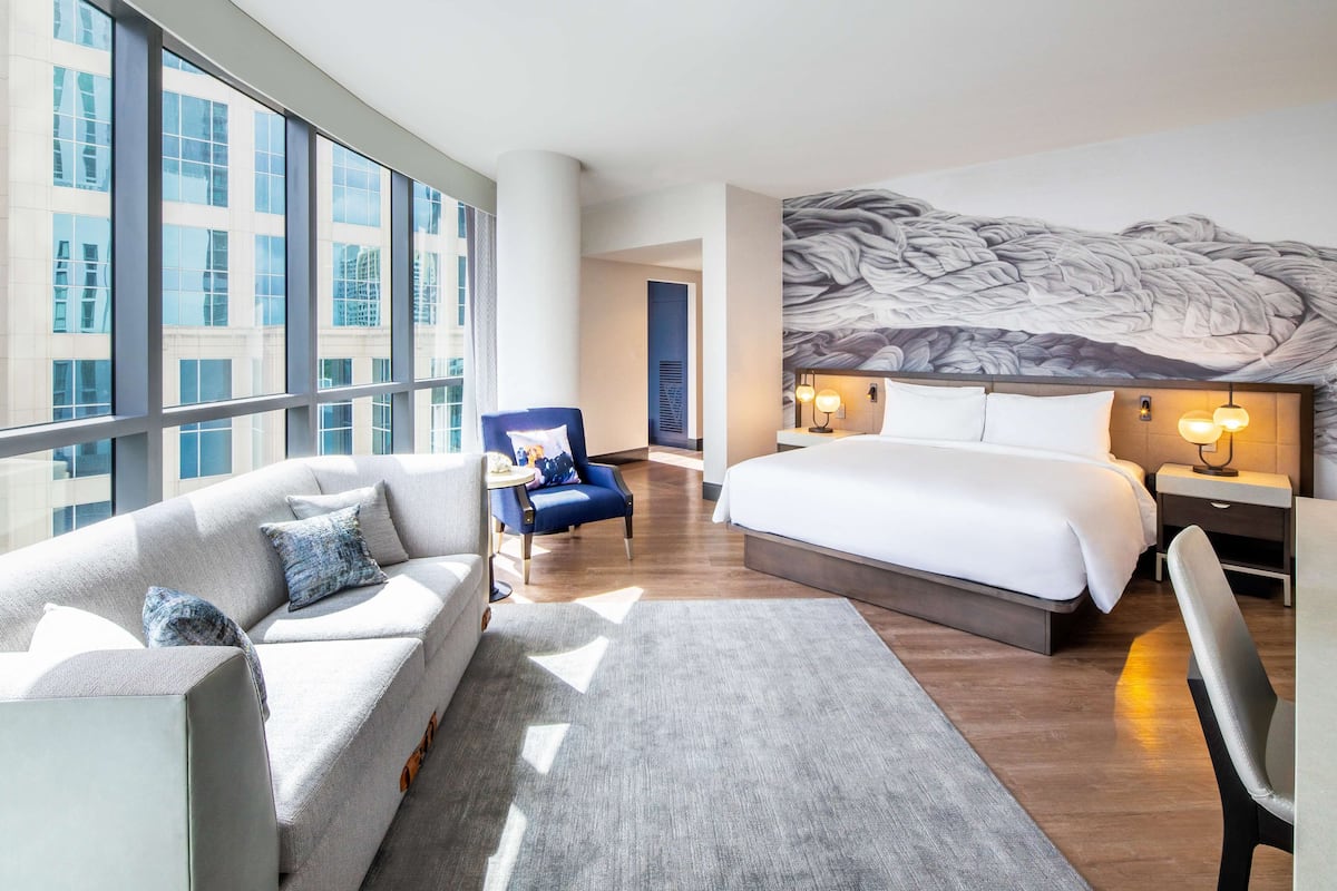 Een moderne hotelkamer met een groot bed, een bank, een stoel en een raam met uitzicht op de stad.