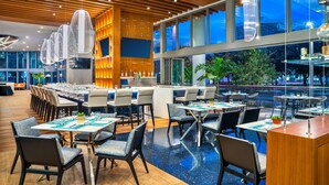 A modern restaurant with a wooden ceiling, large windows, and a variety of seating arrangements.