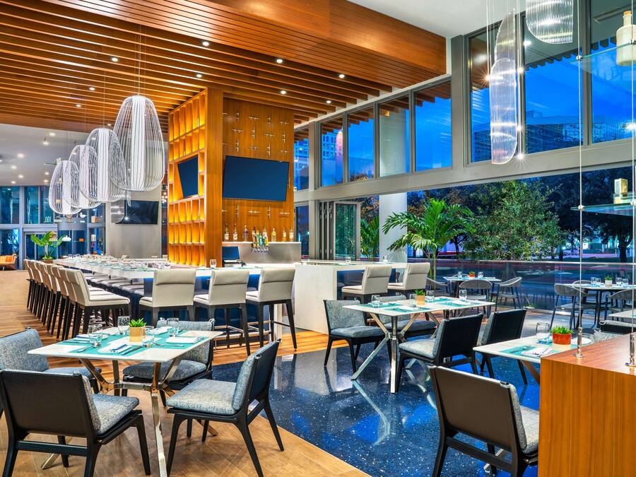 A modern restaurant with a wooden ceiling, large windows, and a variety of seating arrangements.