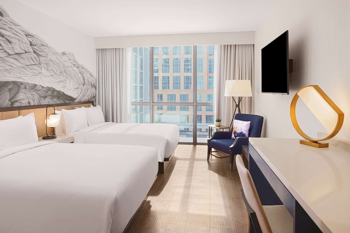 Een hotelkamer met twee bedden, een televisie, een bureau en een groot raam met uitzicht op de stad.