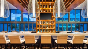 A modern bar area with a long counter, multiple bar stools, and a display of liquor bottles.