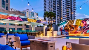 A rooftop bar with outdoor seating, a pool, and a mural.