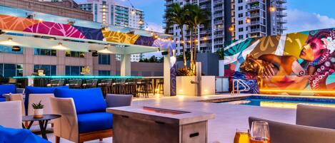 A rooftop bar with outdoor seating, a pool, and a mural.